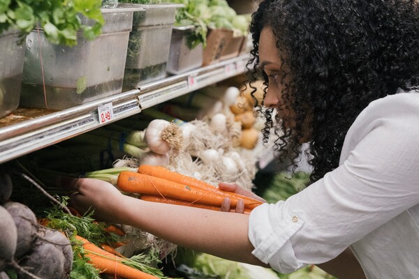 A imagem contém uma mulher na seção de hortifrúti escolhendo alimentos que aumentam a imunidade.