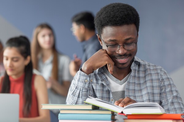 A imagem contém um jovem estudante que sabe como organizar o tempo para estudar, já que lê um livro sorrindo, demonstrando tranquilidade.