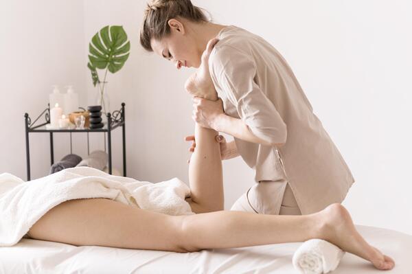 A imagem apresenta uma sessão de fisioterapia dermatofuncional na qual a paciente está deitada na esteira enquanto a fisioterapeuta massageia sua panturrilha direita.