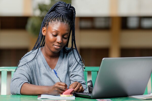 A imagem contém uma jovem fazendo anotações sobre a grade curricular de Medicina após pesquisar em seu computador.