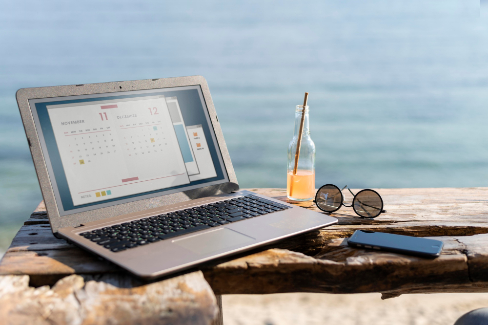 Notebook, óculos escuro e um celular em cima de um banco de frente pro mar. 