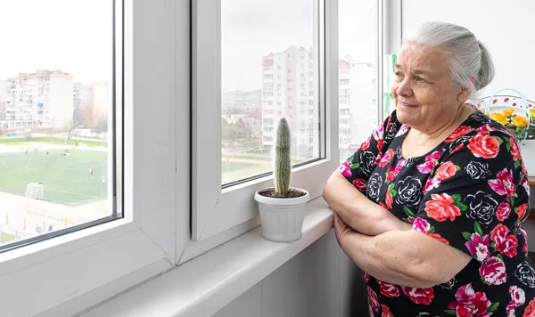 A imagem contém uma senhora olhando sorridente para a paisagem além de sua janela, feliz pela sua qualidade de vida, elemento que influencia no envelhecimento populacional.